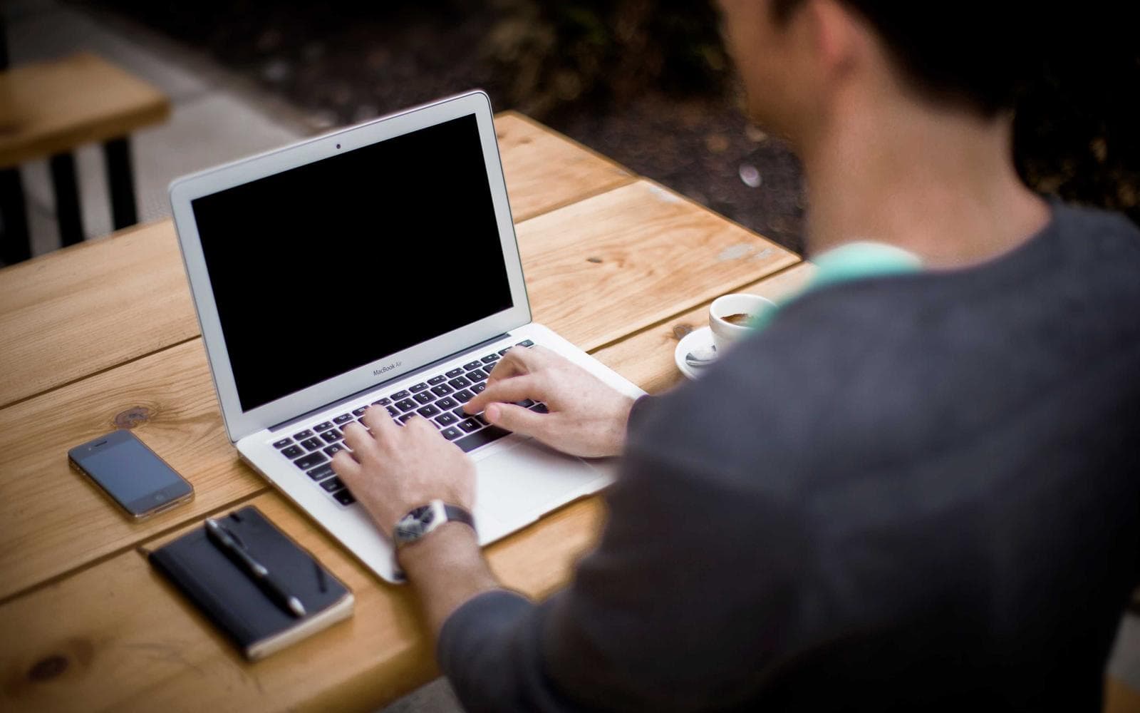 Someone working at a laptop at a wooden desk, seen over the shoulder.