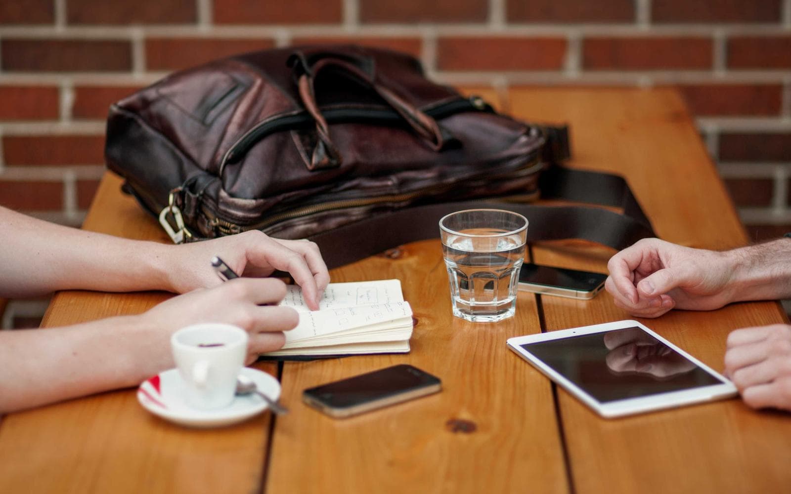 Two people talking across a table with a notebook, a tablet and coffee.